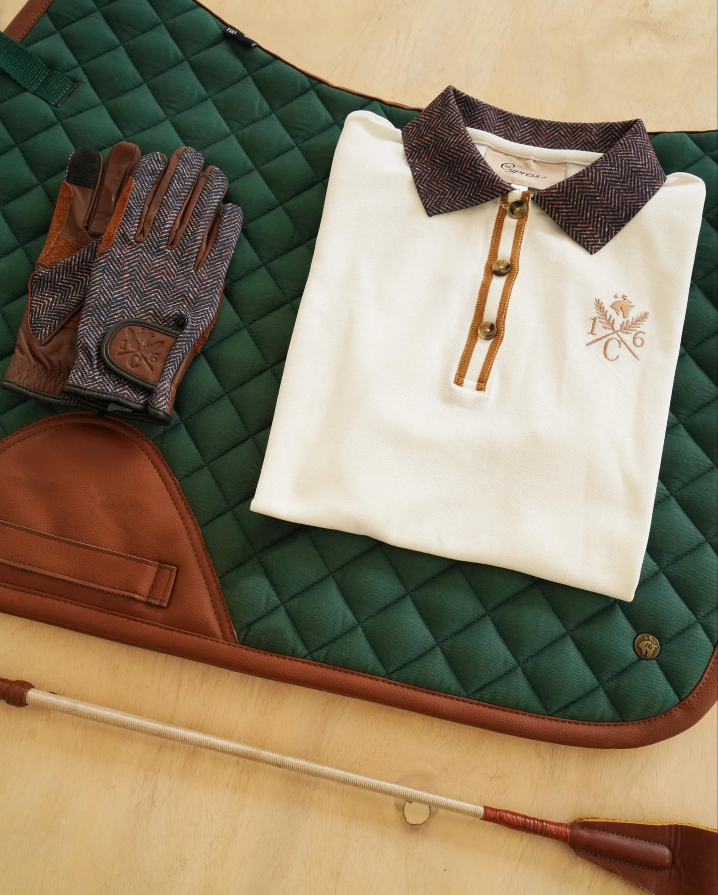 cypress green english saddle pad herringbone gloves white polo shirt and crop on a wooden background