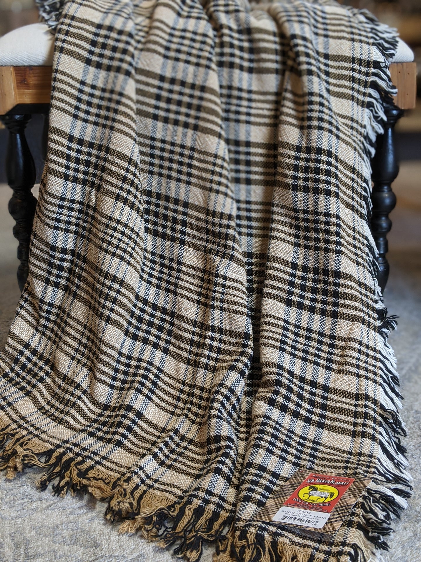 Tan, cream, and navy woven cotton plaid afghan draped over a wooden spindle chair with fringe edges.