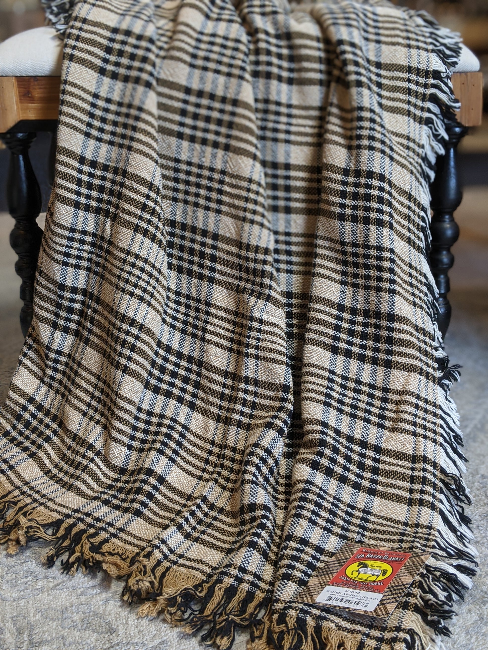 Tan, cream, and navy woven cotton plaid afghan draped over a wooden spindle chair with fringe edges.