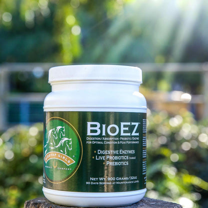 A white plastic jar of BioEZ Digestive Support supplement by Healthy Girls Energy Company, set on a wooden surface with a blurred green garden background.