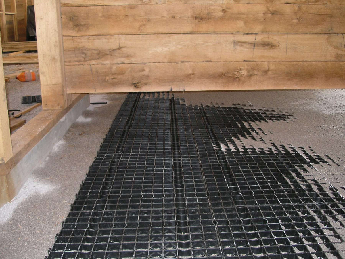 Stall Grid flooring system shown during installation, with reinforced grid panels set against a wooden stall frame.