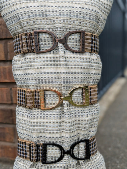 Three Limited Edition 5/A Baker × Ellany elastic belts displayed on a woven mannequin stand, each featuring signature Baker plaid and a different metal buckle finish—copper, gold, and matte black—with “ELLANY” engraved on each buckle.