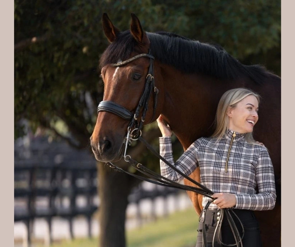 Rider standing beside a horse while wearing the Baker × Novella plaid quarter zip and dark riding pants.