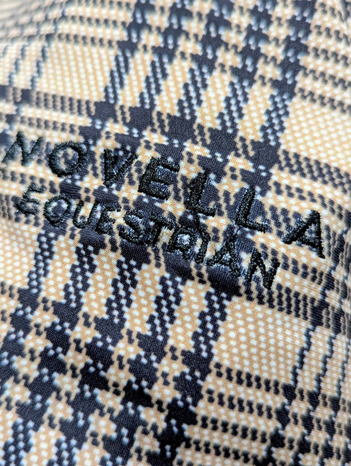 Close‑up of the Baker × Novella plaid fabric with NOVELLA EQUESTRIAN embroidered branding.