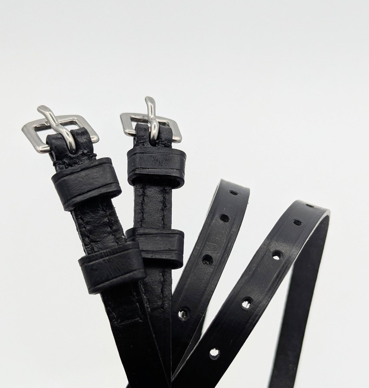 Multiple black leather spur straps arranged on a white background, highlighting smooth leather, stitched edges, adjustment holes, and square metal buckles.