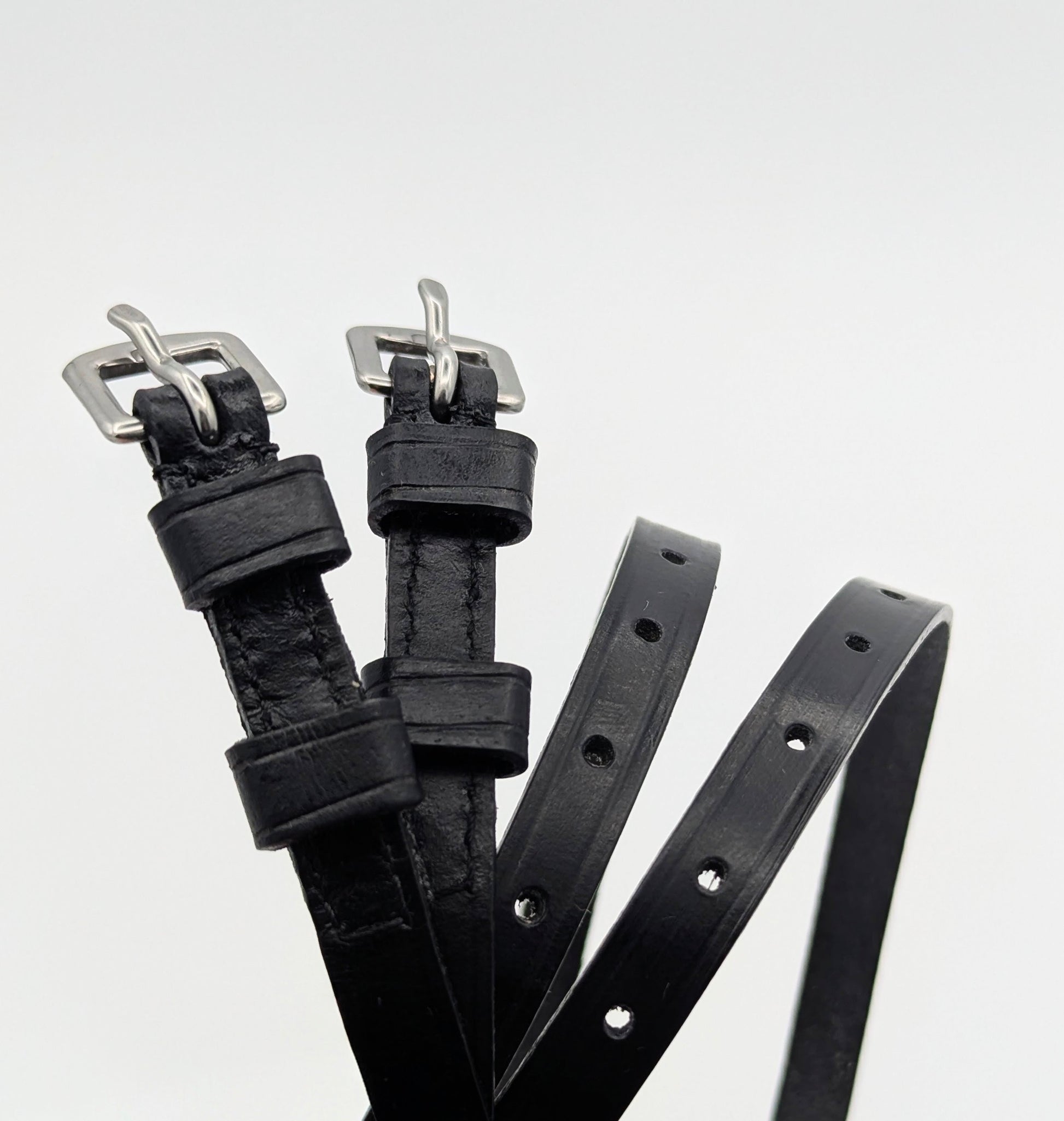 Multiple black leather spur straps arranged on a white background, highlighting smooth leather, stitched edges, adjustment holes, and square metal buckles.