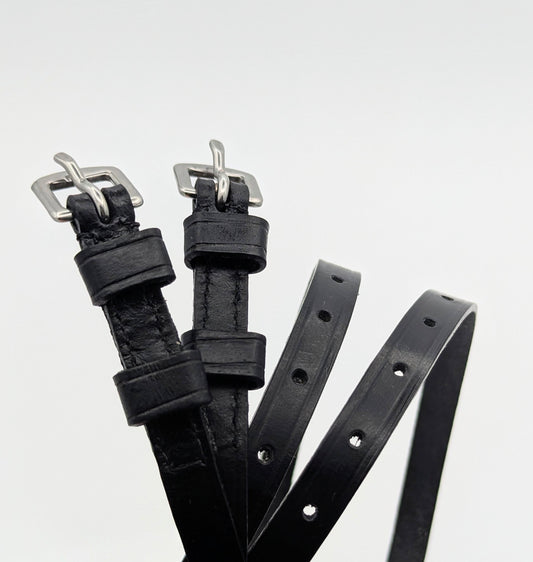 Multiple black leather spur straps arranged on a white background, highlighting smooth leather, stitched edges, adjustment holes, and square metal buckles.