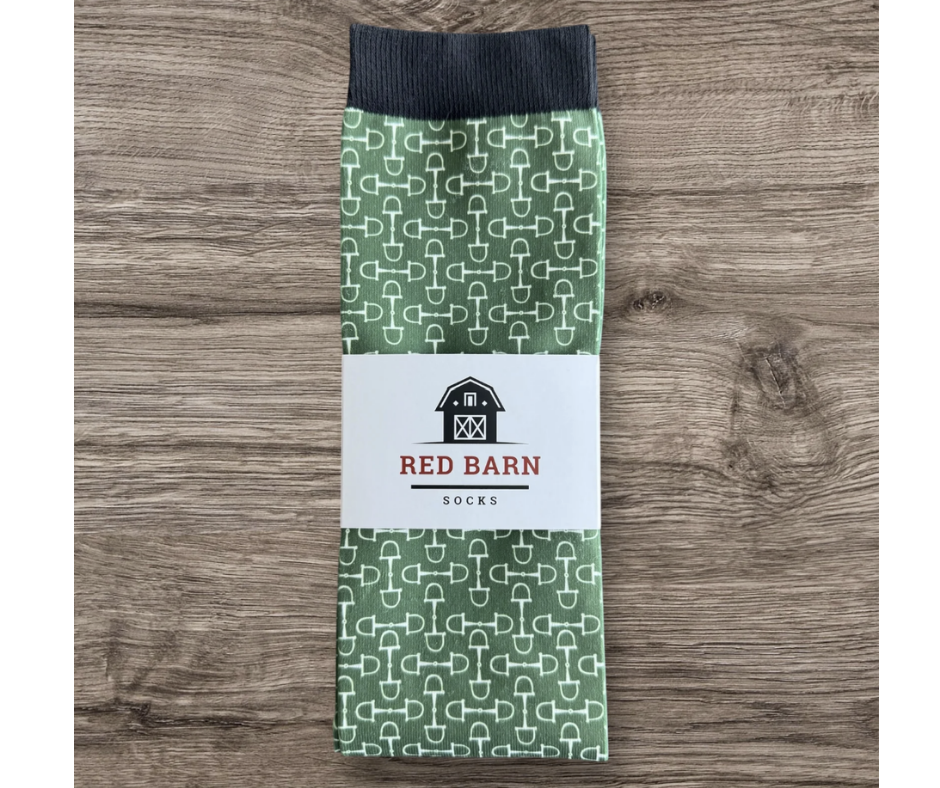 Green tall socks with white bit pattern and black footbed wrapped in a Red Barn Socks label on a wooden surface