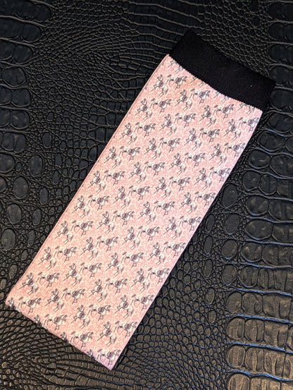 Pink horse‑pattern sock with black cuff displayed on a textured black surface