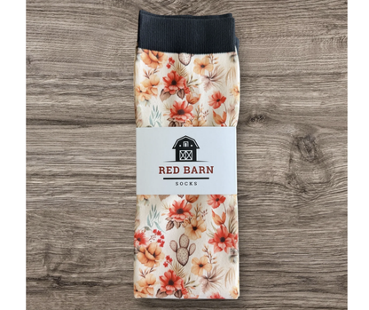 A pair of folded socks with a floral print and a black ribbed cuff, wrapped in a white paper band labeled 'RED BARN SOCKS', displayed on a gray wood background.