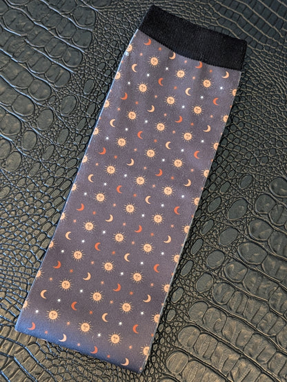 Navy sock with celestial sun, moon, and star pattern and black cuff displayed on a textured black surface