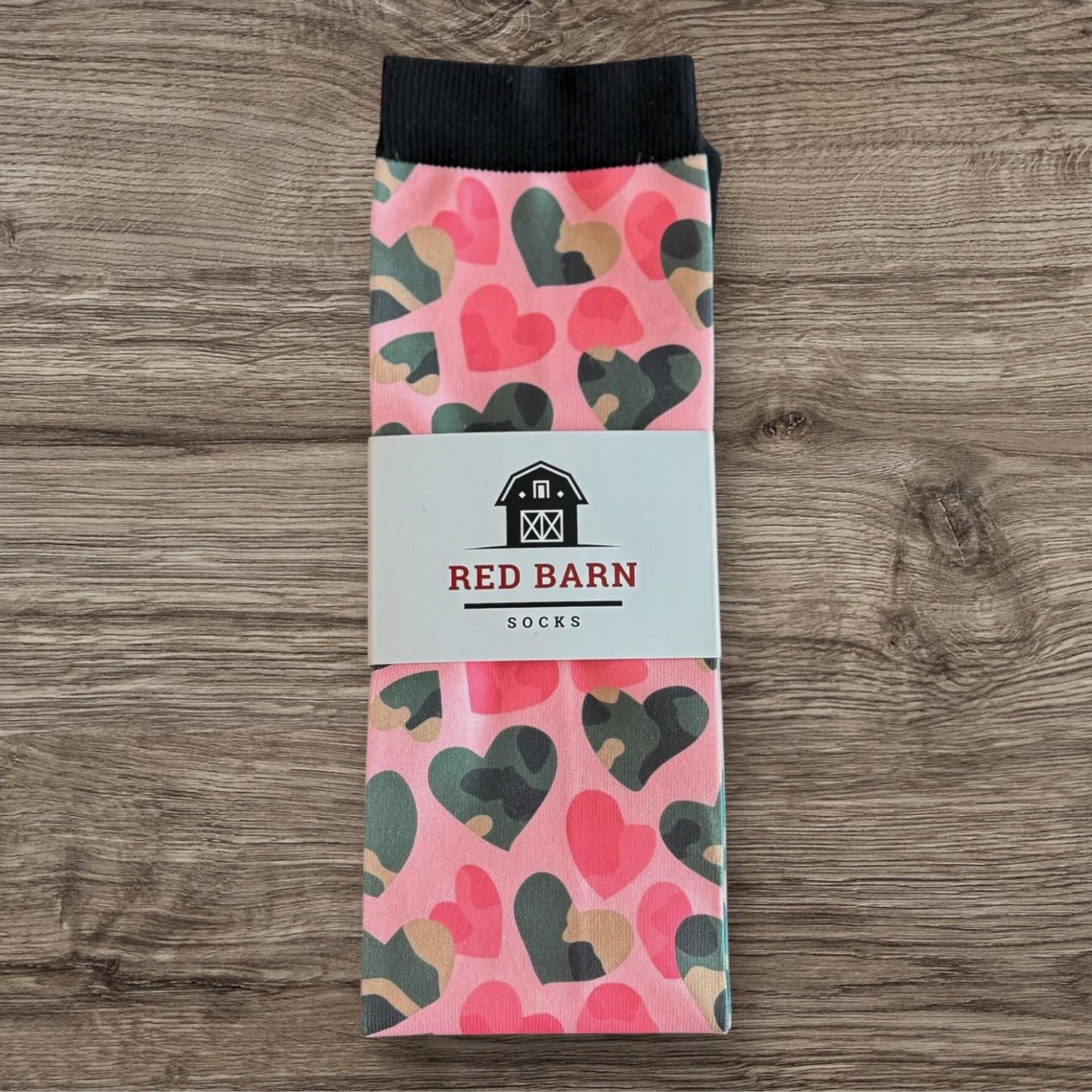 Pink tall socks with multicolor heart pattern and Red Barn Socks label, folded on a wooden surface