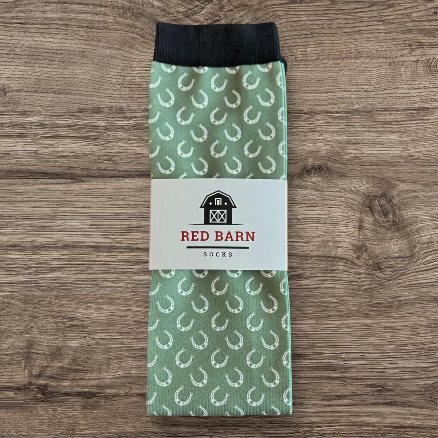 Sage green tall socks with white horseshoe pattern and Red Barn Socks label, folded on a wooden surface