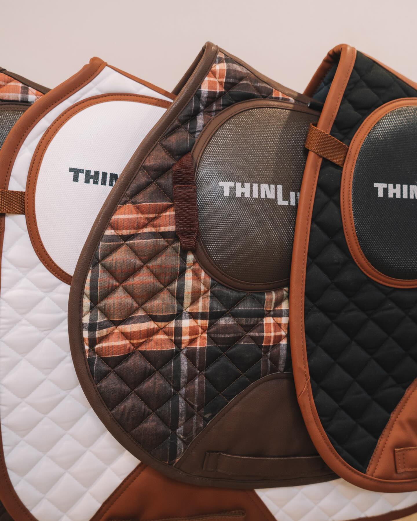 three different sixteen cypress and thinline english saddle pads on display with a cream background.