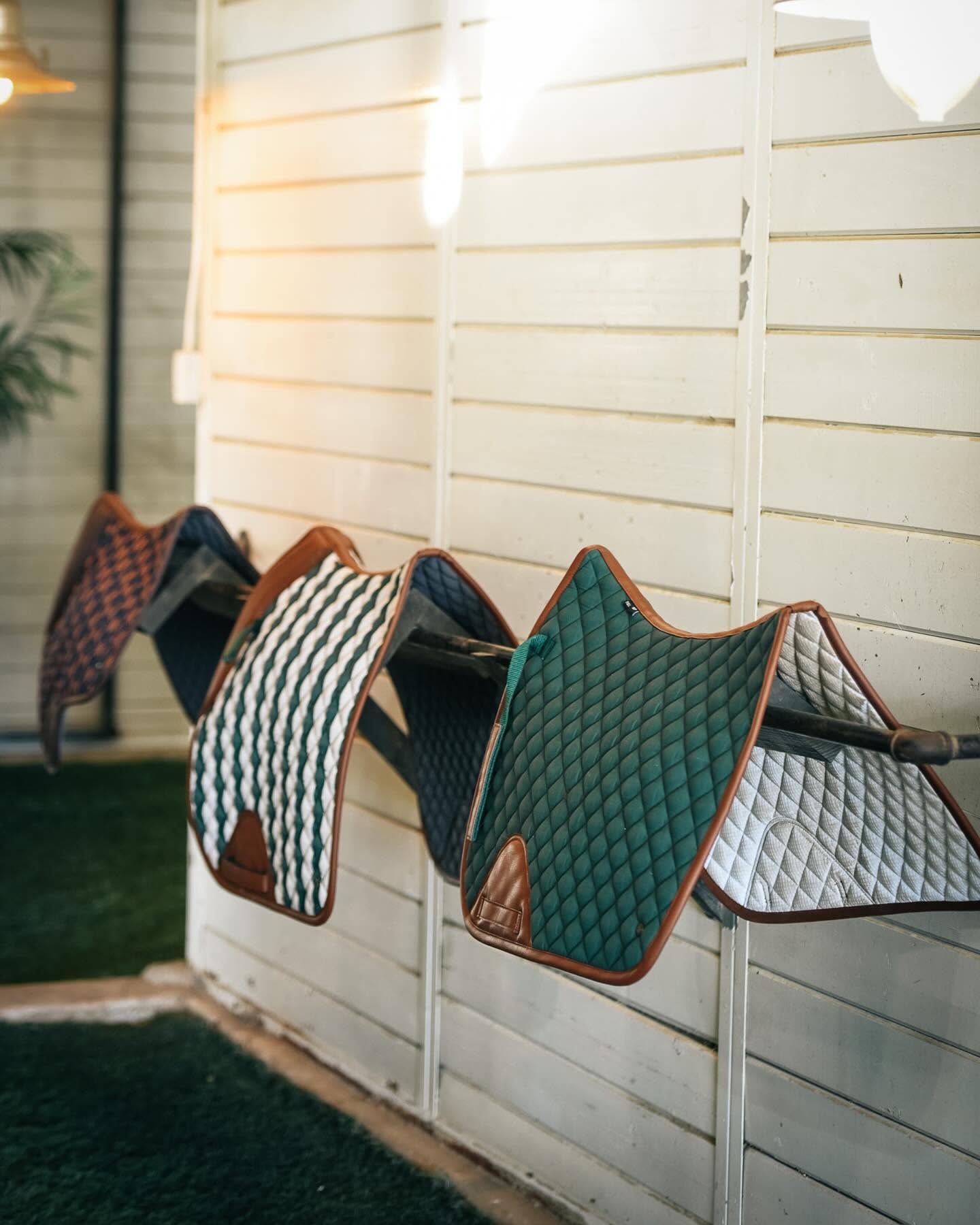 various sixteen cypress english saddle pads on a bar next to a white wooden wall
