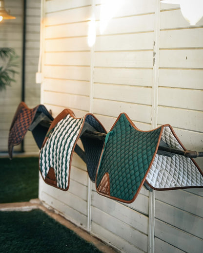 various sixteen cypress english saddle pads on a bar next to a white wooden wall
