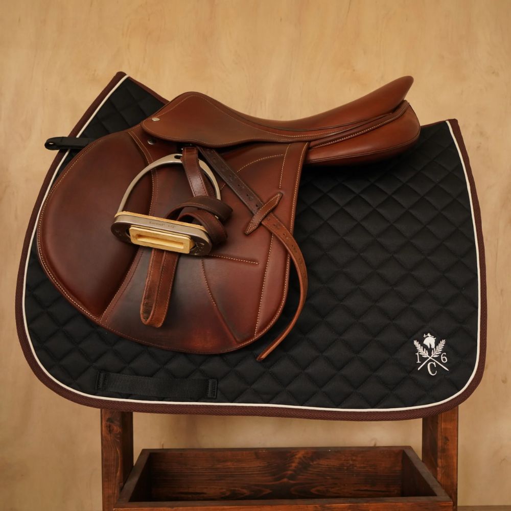 Black diamond‑quilted saddle pad with ivory piping and embroidered 16C crest on wooden stand