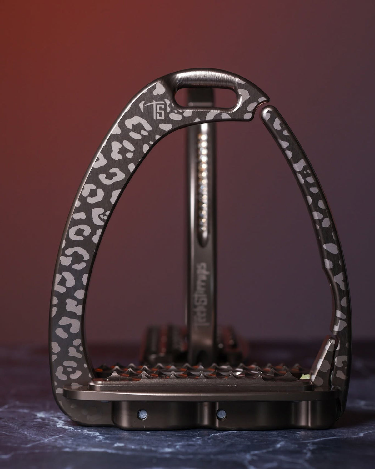 Brown Italian‑made safety stirrups with warm leopard pattern and wide spiked tread, displayed against a red gradient background.