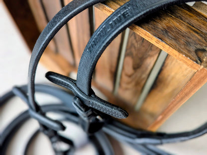 Close‑up of black ThinLine English reins draped over a wooden crate, highlighting the stitching, leather detail, and buckle end construction.