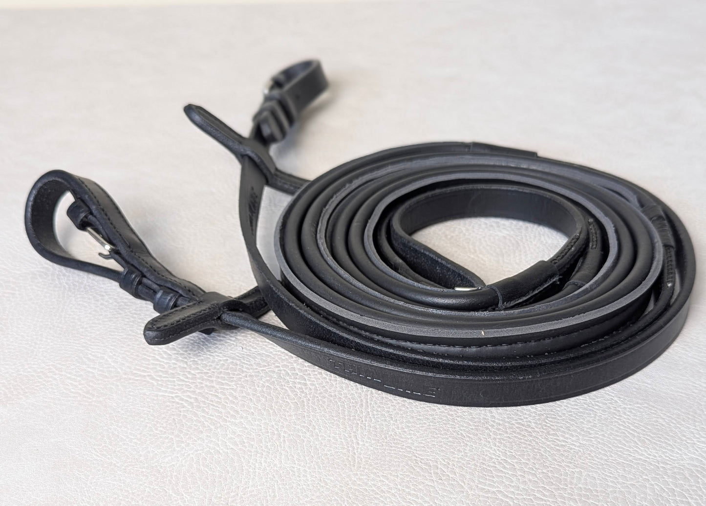 Coiled black ThinLine Smooth English reins on a light textured surface, showing the buckle ends and smooth wrapped grip material.