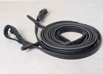 Coiled black ThinLine Smooth English reins on a light textured surface, showing the buckle ends and smooth wrapped grip material.