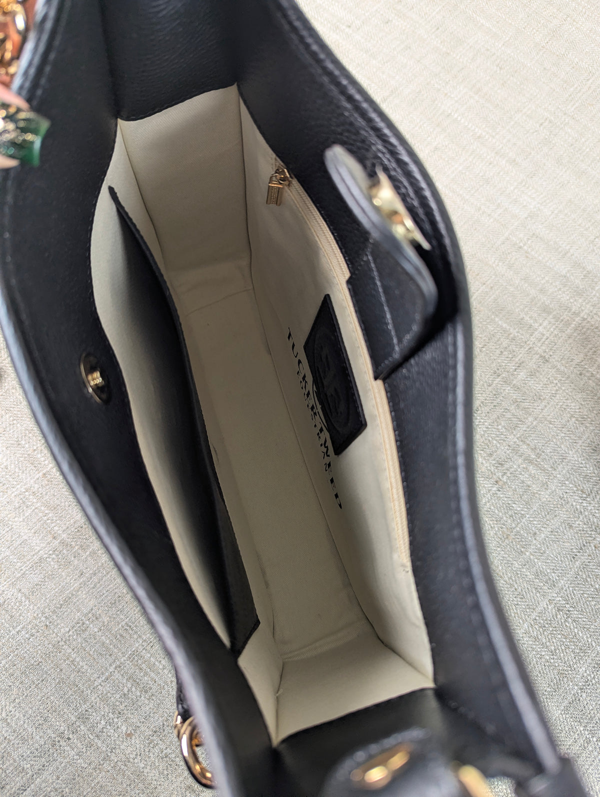 Interior of the Tucker Tweed Middleburg Messenger purse showing the light beige lining, gold hardware, interior zip pocket, and branded leather patch.
