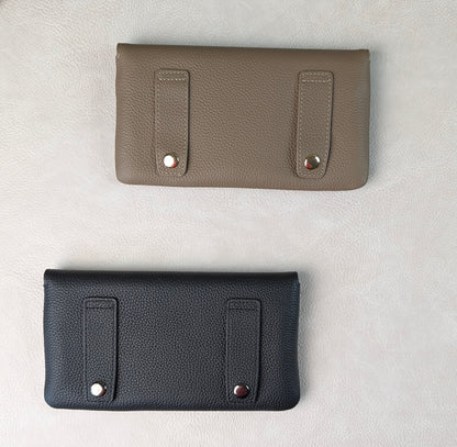 Two pebbled leather tucker tweed stablemate belt bag accessories laid flat on a light textured background, one in taupe and one in black, each with two vertical strap details and metal snap hardware for belt loops.