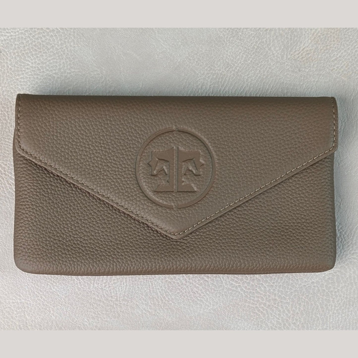 A stone brown grey tuape pebbled leather envelope belt bag with a circular embossed logo featuring a balance scale, displayed on a light gray textured background.