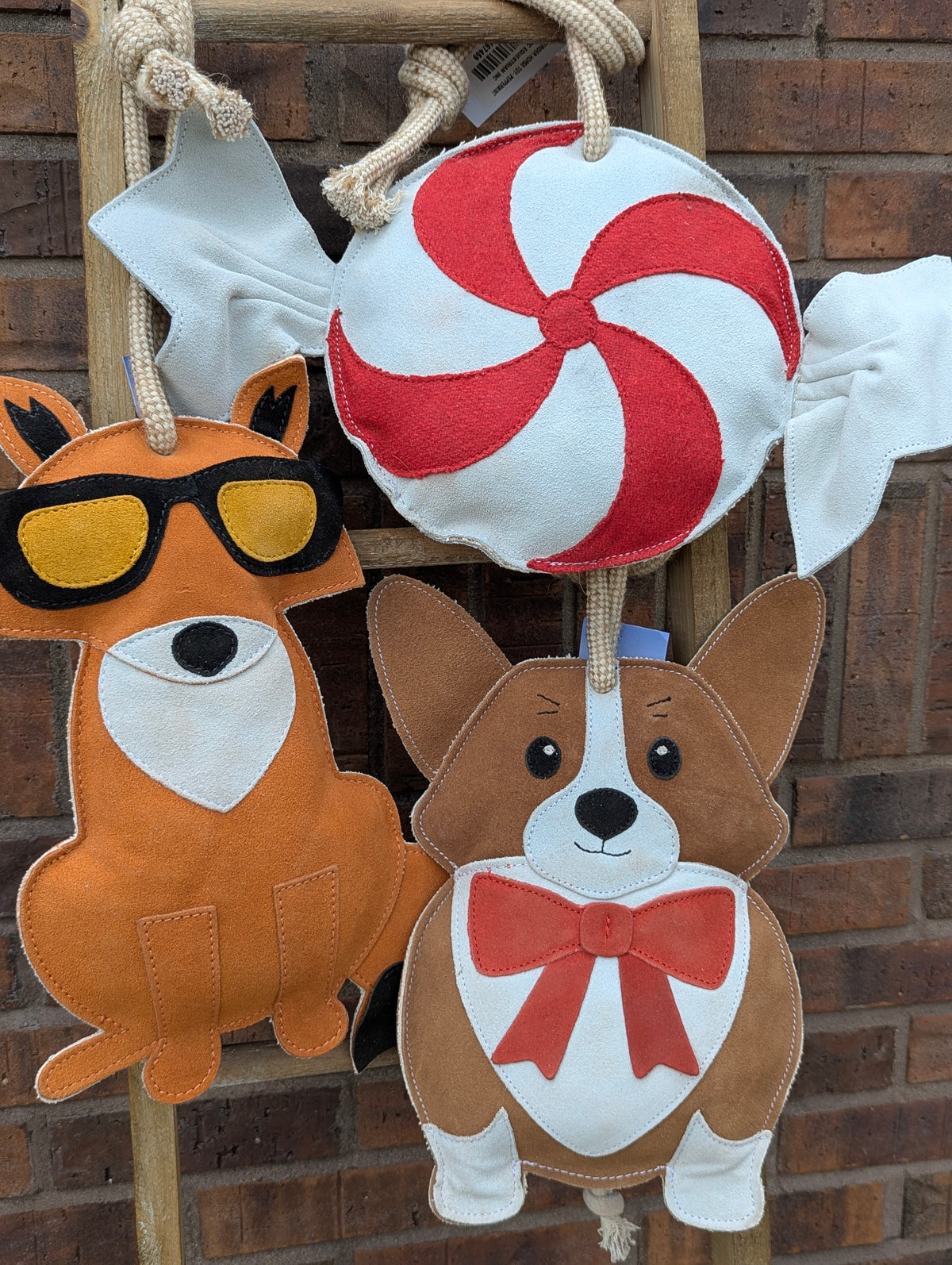 Three TuffRider stall toys hanging on a wooden ladder: peppermint candy, fox, and corgi designs.