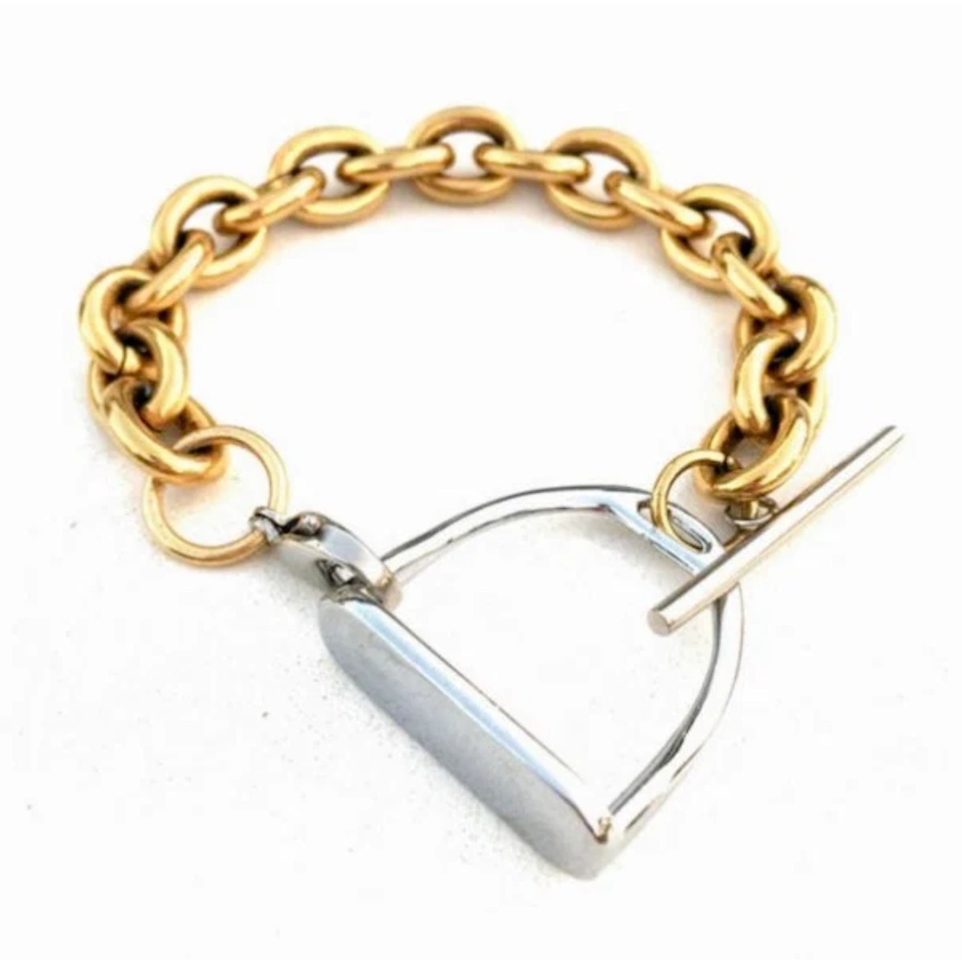 Two‑tone equestrian stirrup bracelet with chunky gold chain links and a silver stirrup‑style clasp displayed on a light marble surface.