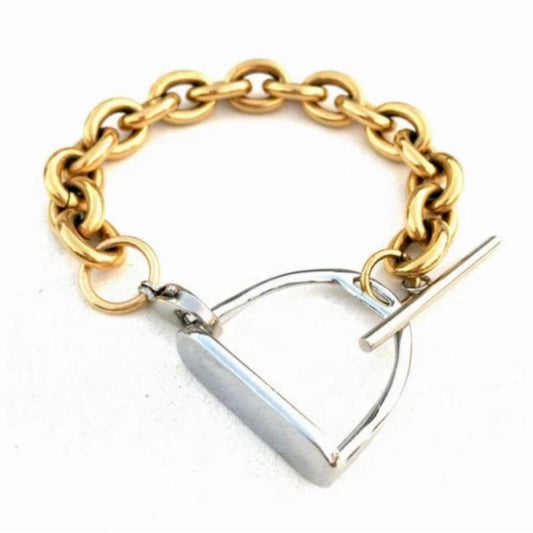 Two‑tone equestrian stirrup bracelet with chunky gold chain links and a silver stirrup‑style clasp displayed on a light marble surface.